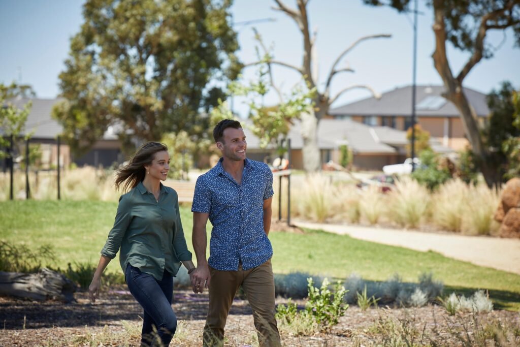 A young couple standing in front of their new, affordable home, smiling and holding a brochure about house and land packages.